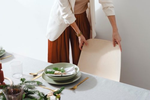 Unrecognizable female hands setting up Christmas table in dinning room.