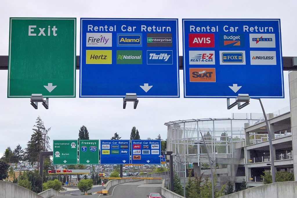 Signs directing airline passengers to different car rental services at the airport.
