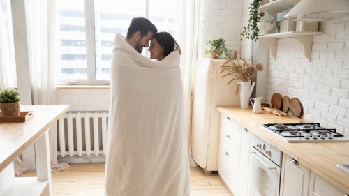young couple standing in kitchen wrapped in a warm blanket