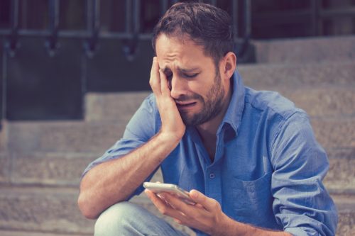 man crying while reading a break up text message on his phone