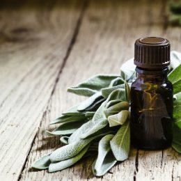 A bottle of sage oil surrounded by sage leaves on a wooden table