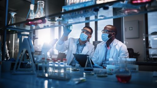 Phòng thí nghiệm nghiên cứu y học hiện đại: Hai nhà khoa học đeo khẩu trang sử dụng kính hiển vi, phân tích mẫu trong đĩa Petri, thảo luận về công nghệ đổi mới.  Phòng thí nghiệm khoa học tiên tiến về y học, công nghệ sinh học