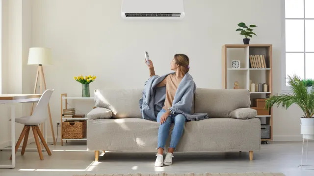 Woman at home on couch turning on air conditioner