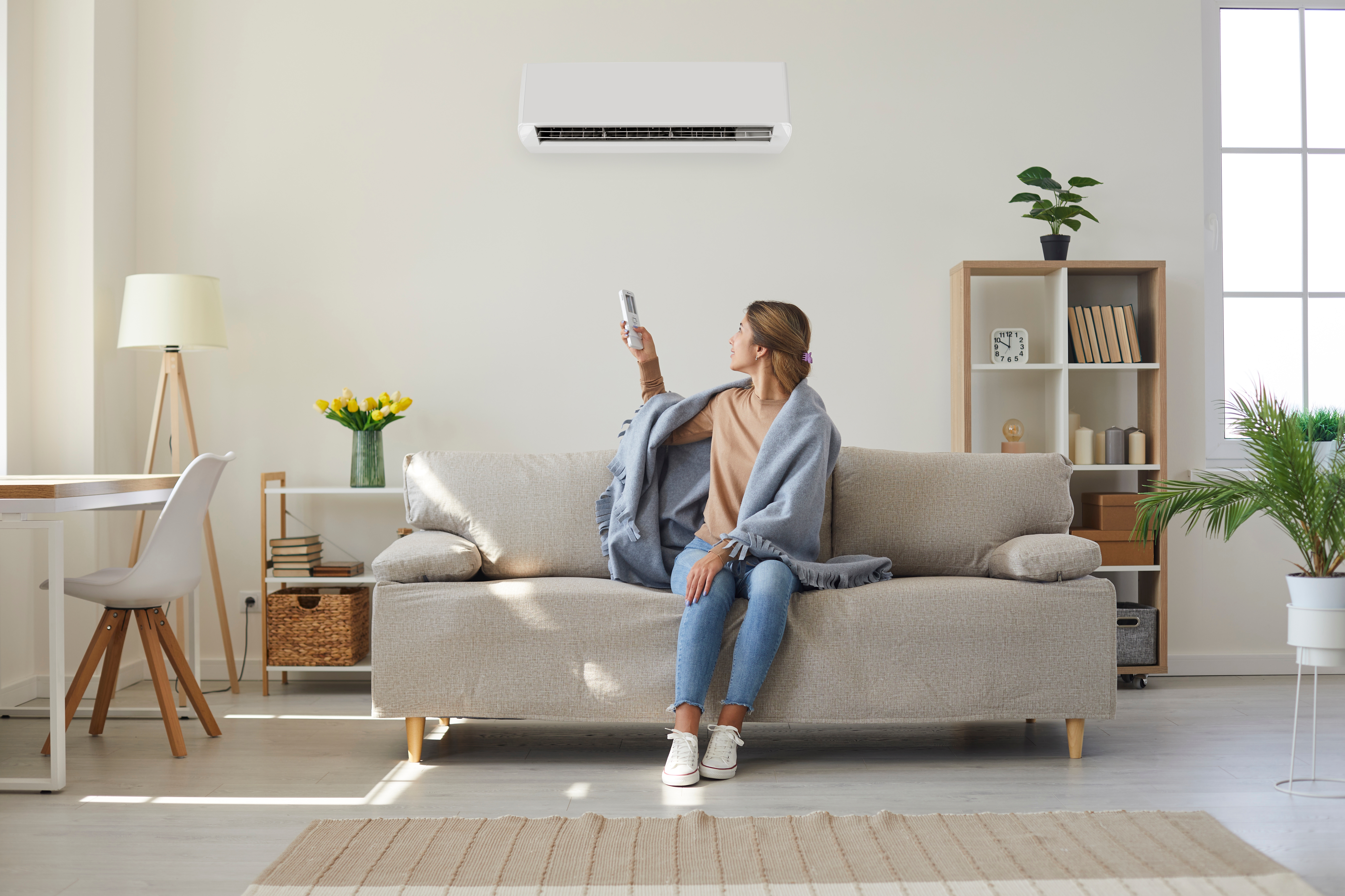 Woman at home on couch turning on air conditioner
