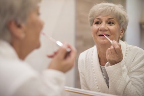older woman putting on lip gloss