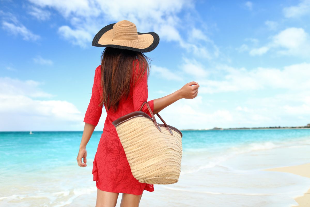 Woman in red on beach with bag and hat