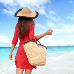 Woman in red on beach with bag and hat