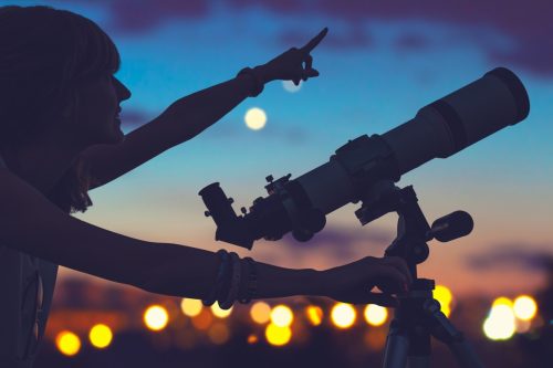 woman with a telescope pointing at the night sky