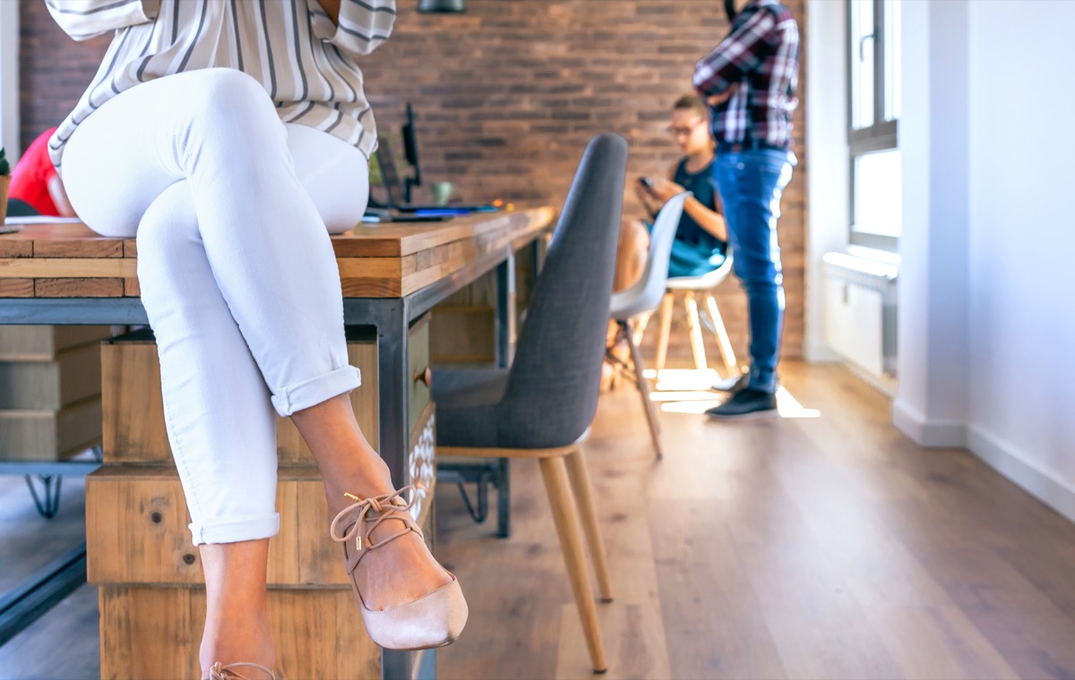 Unrecognizable businesswoman sitting on table in the office with colleagues working in the background