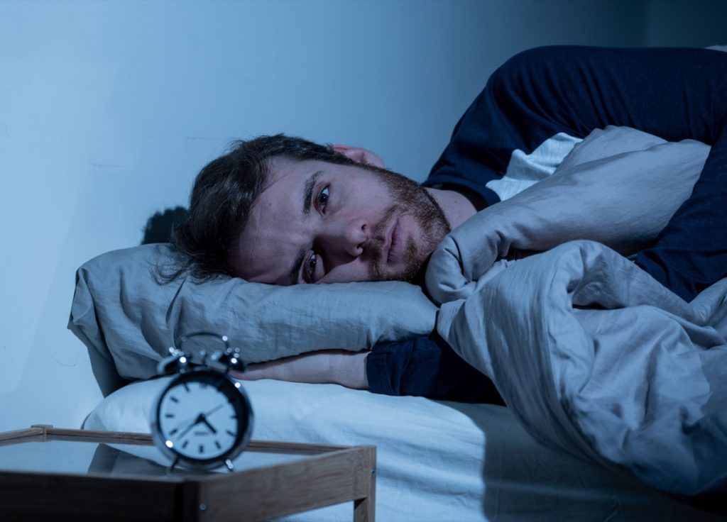Sleepless man awake at night not able to sleep, looking at clock suffering from insomnia