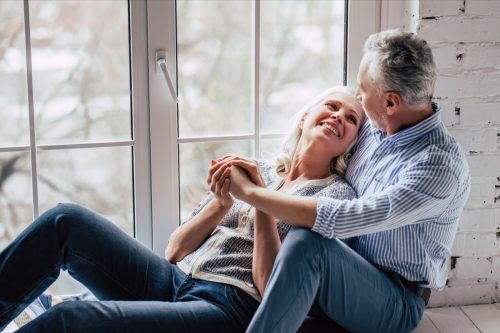 older man and woman cuddling by the window