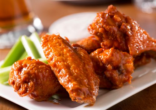A plate of buffalo style chicken wings with celery and blue cheese with a beer on a bar or restaurant table. Please see my portfolio for other food and drink images.