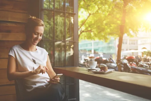người phụ nữ mỉm cười trong quán cà phê khi đọc tin nhắn từ bạn trai