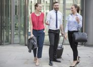 Two female coworkers and a male walking out of a glass office building.