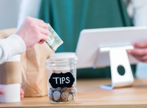 Close up of a someone putting a dollar into a tip jar next to a cash register