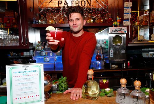 Tom Schwartz behind the bar holding out a cocktail at a Patron event