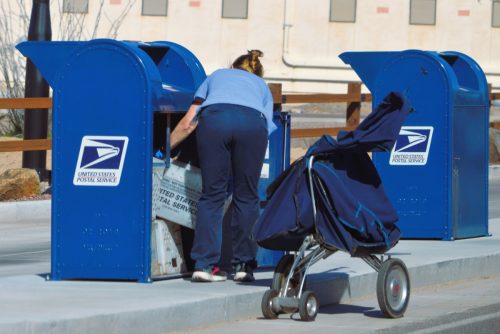 Ngày 04 tháng 4 năm 2023: Một nhân viên bưu điện của USPS thu thập thư gửi đi tại hộp chuyển phát drive-thru.