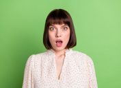 young woman looking shocked after learning weird facts - green background