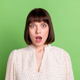 young woman looking shocked after learning weird facts - green background