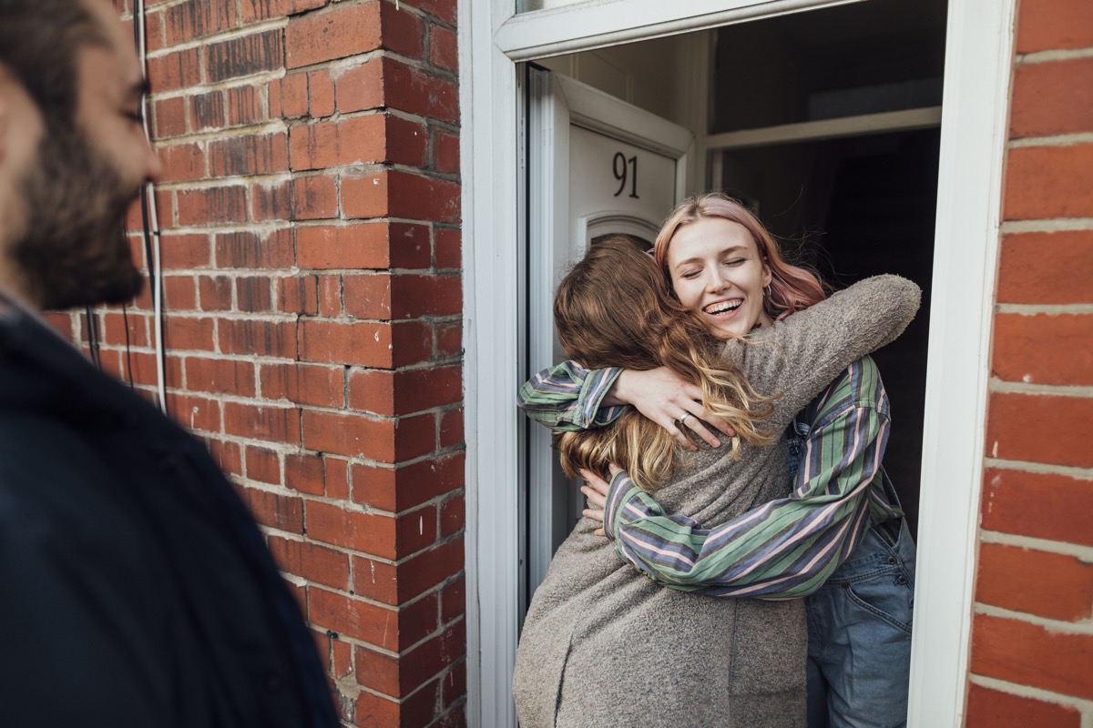 Friends arriving at a house for a social gathering. They are greeting each other at the front door.