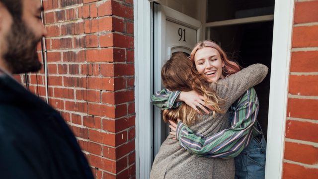 Friends arriving at a house for a social gathering. They are greeting each other at the front door.