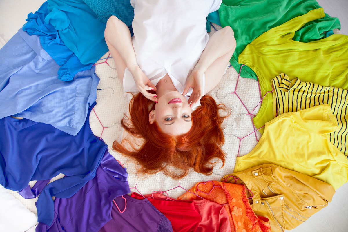 Top view of a woman with red hair laying on her bed surrounded by a circle of colorful clothes