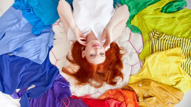 Top view of a woman with red hair laying on her bed surrounded by a circle of colorful clothes