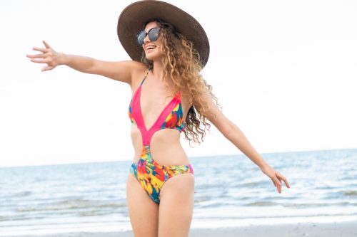 A happy young woman on the beach, wearing a monokini swimsuit and sun hat