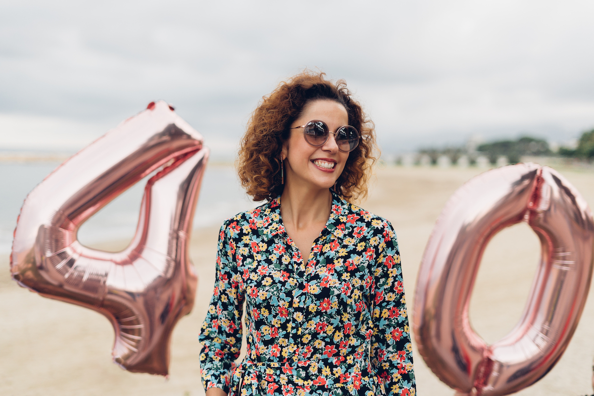 Attractive curly brunette celebrating her 40th birthday with big balloons on the beach