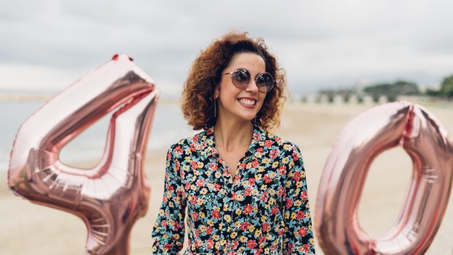 Attractive curly brunette celebrating her 40th birthday with big balloons on the beach