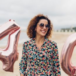 Attractive curly brunette celebrating her 40th birthday with big balloons on the beach