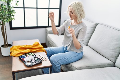 A young blonde woman on her couch about to sew a yellow shirt.