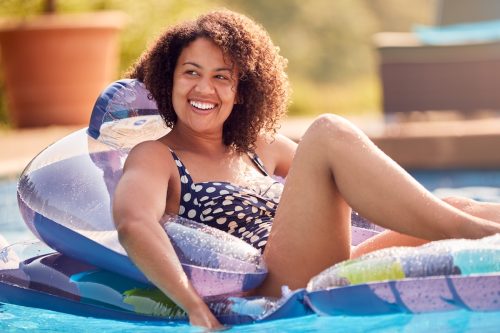 A smiling woman on a float in a pool, wearing a polka dot bathing suit