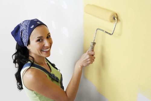 Elevated portrait view of a happy woman with roller applying yellow paint on a wall
