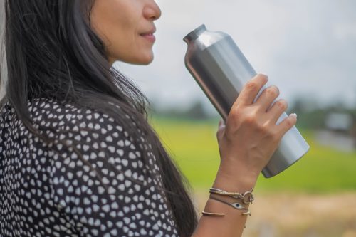 Close-up shot of a tourist drinking water from a reusable stainless steel bottle while looking at the view.