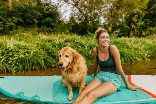 Photo of a young woman and her dog sitting on the paddleboard