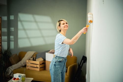 A young, smiling woman paints her walls a sage green color.