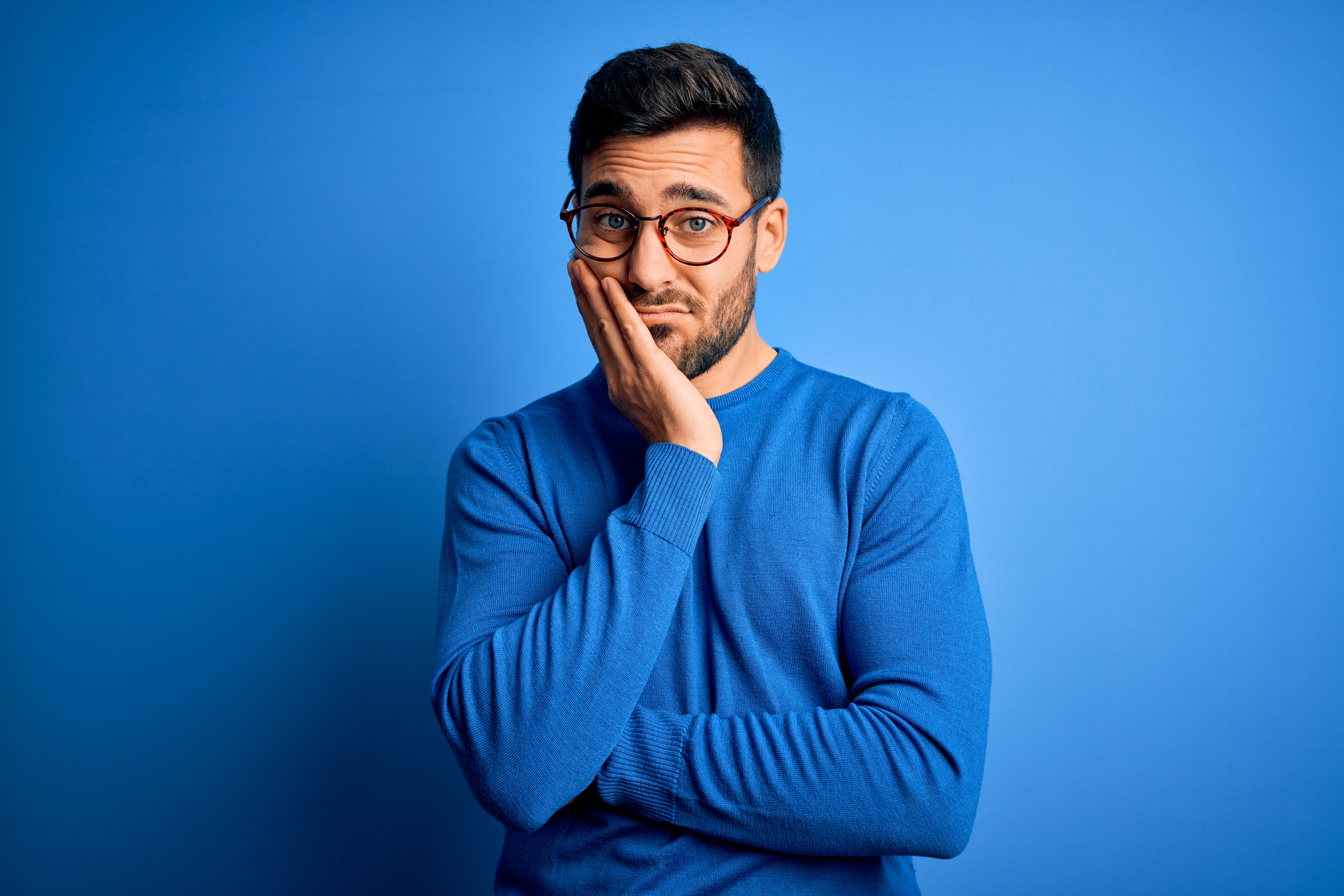 Young unhappy man wearing blue with blue background