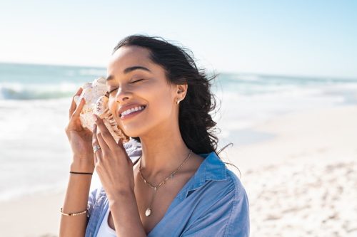 Woman Listening to Seashell on the Beach