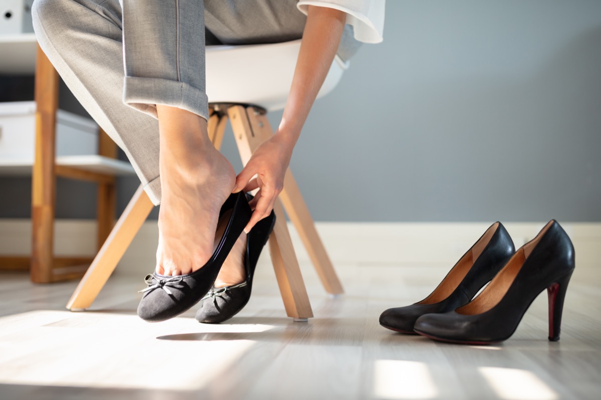 Low Section Of Businesswoman Changing Footwear From High Heel To Comfortable Shoes In Office