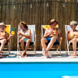Group of cheerful seniors sitting by swimming pool outdoors in backyard.