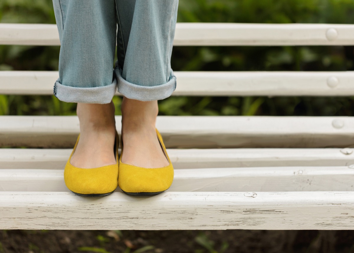 Chân nữ mặc quần jean xanh và giày vàng trên băng ghế trắng.  tập trung có chọn lọc.