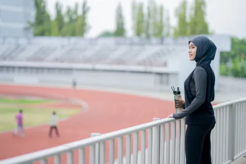 Một phụ nữ Hồi giáo trẻ mặc khăn trùm đầu màu đen tập thể dục trên đường đua gần đó