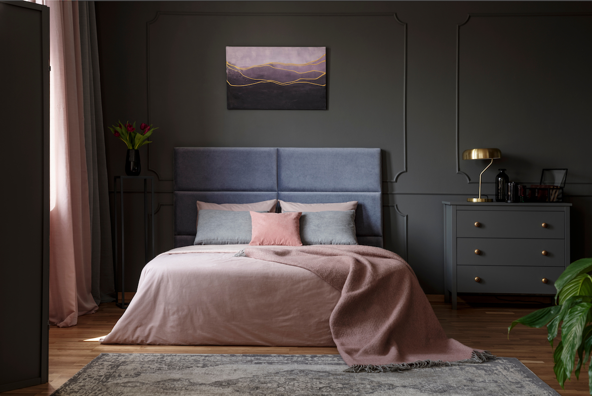 Pastel blanket on bed in pink and blue bedroom interior with gold lamp on grey cabinet
