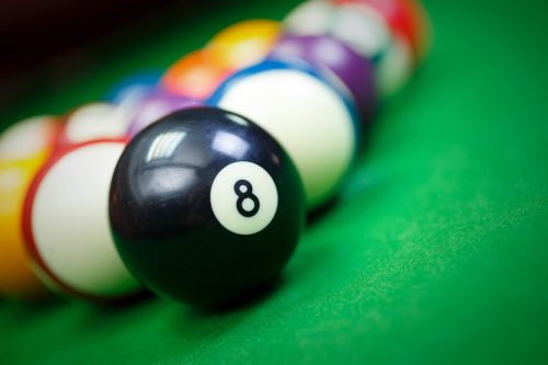Black eight ball on a green pool table with other color balls in the background