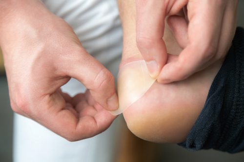 Close up of man's hands putting a blister bandaid on his heel