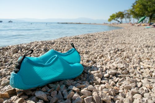Close up of a pair of turquoise blue water shoes on a rocky shore at the beach