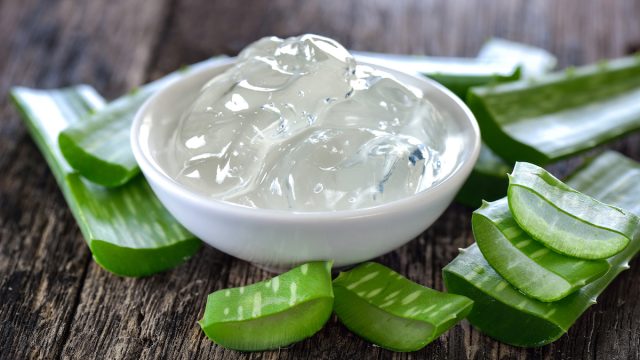 aloe vera gel in bowl with pieces of aloe plant surrounding it on wooden table