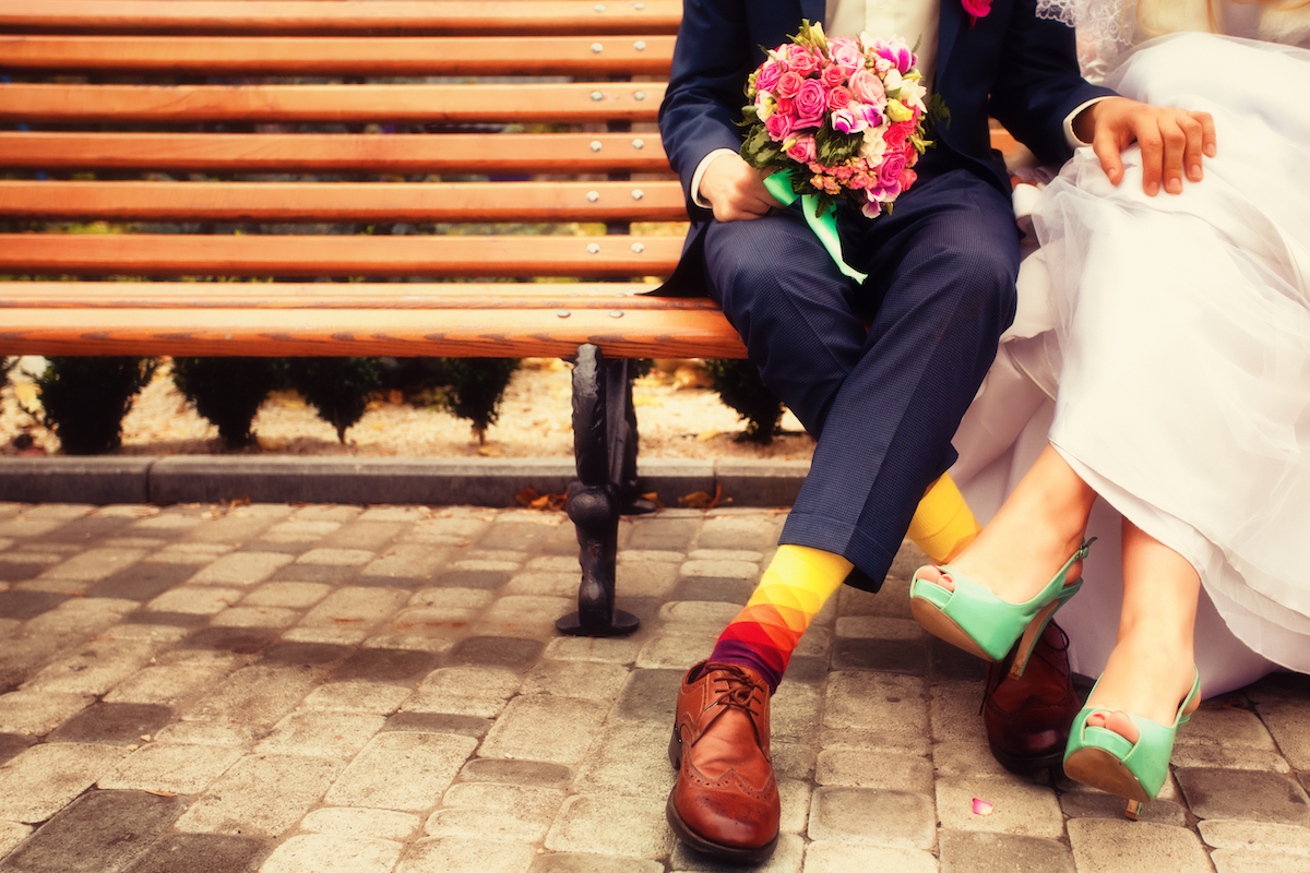 Chest-down view of a bride and groom on a bench wearing colorful shoes and socks