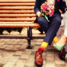 Chest-down view of a bride and groom on a bench wearing colorful shoes and socks